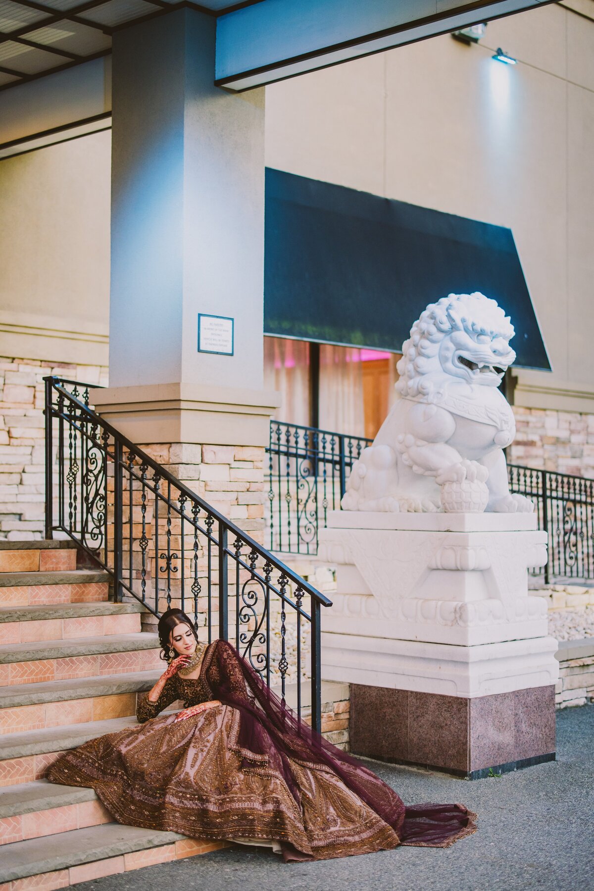 Indian bride sitting on the steps at her sangeet jaago near a lion statue at the deewan banquet in piscataway nj