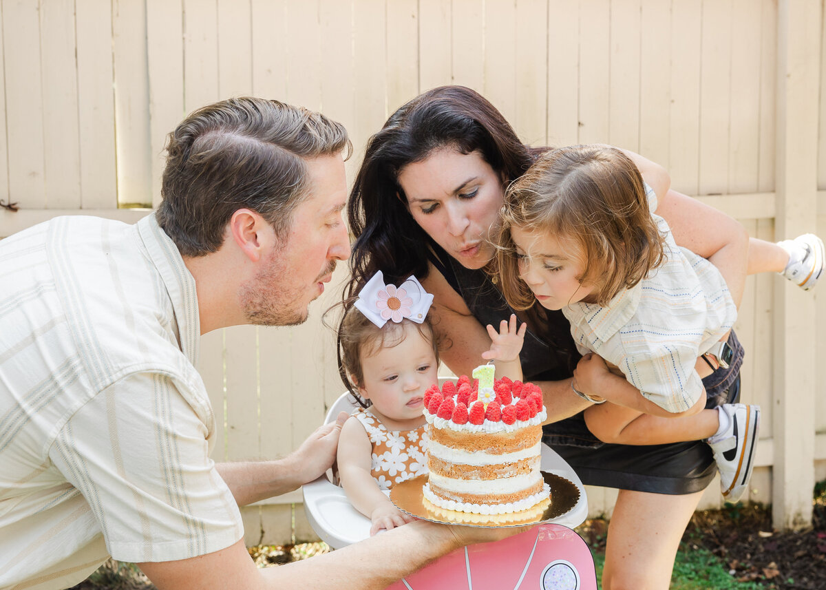 Family blowing out candles on first birthday cake