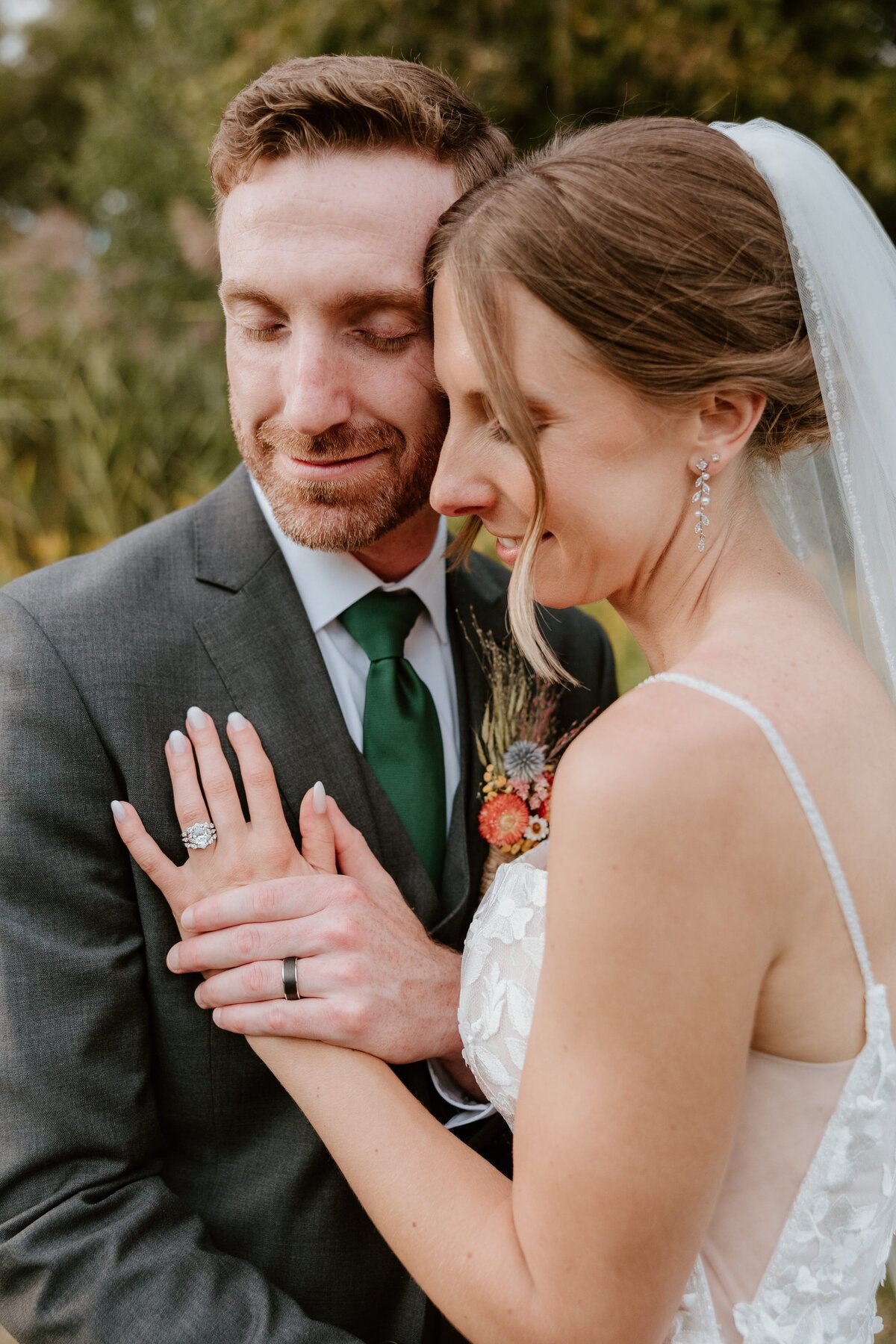 Bride and groom embrace on their wedding day, showing the bride’s engagement ring and lace gown as they lean in with eyes closed.