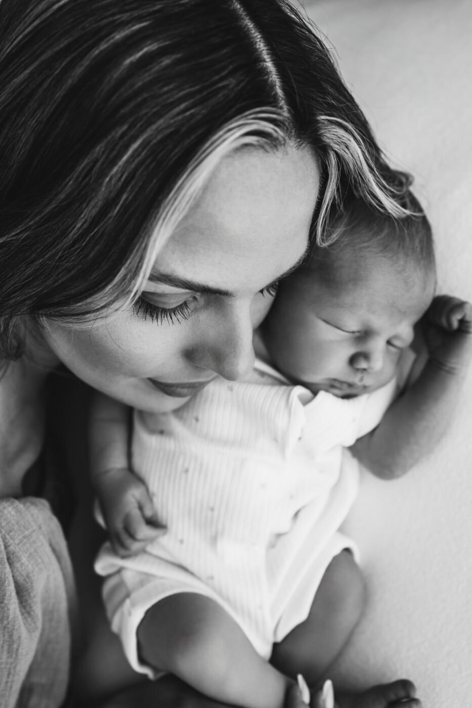 Black and white photo of a mother gently touching her forehead to her sleeping newborn baby's head.