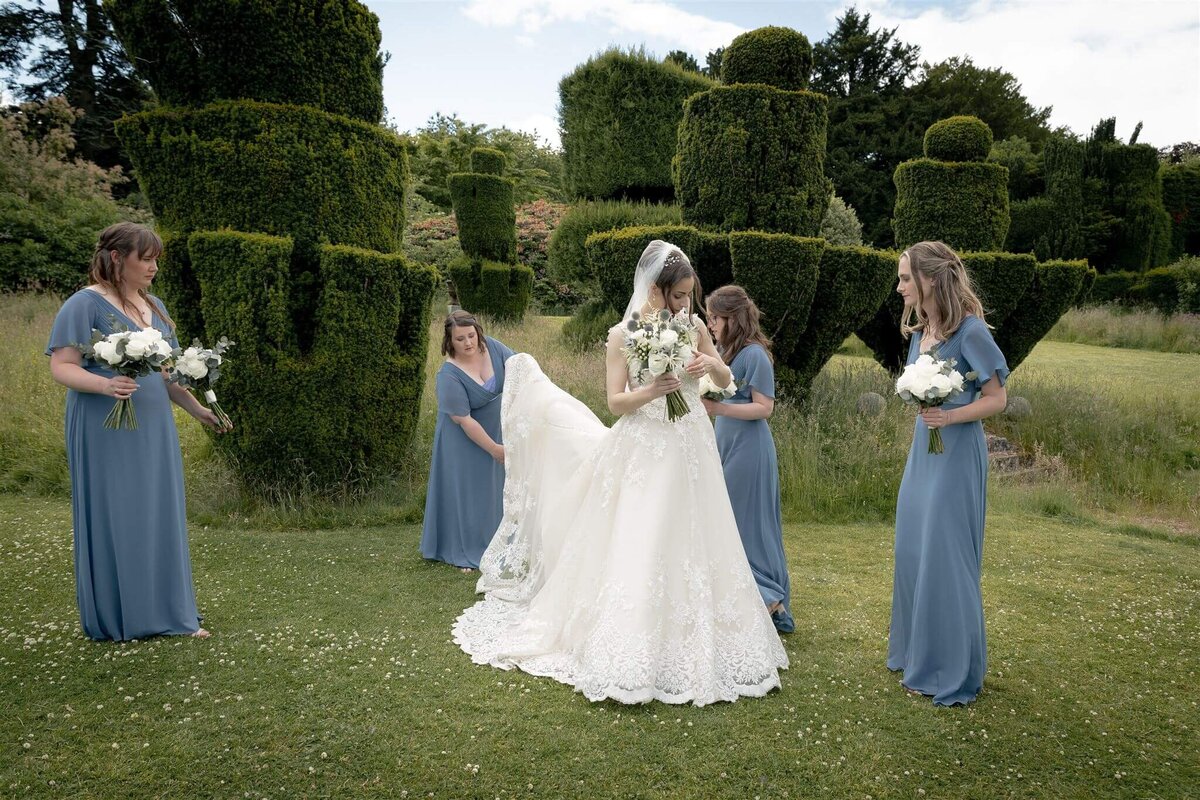 Four bridesmaids in sky blue prepare the bride for external photos in the castle grounds.
