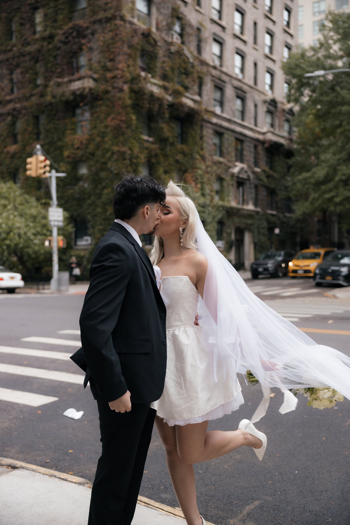 Couple standing close together on a sidewalk as city traffic moves behind them.