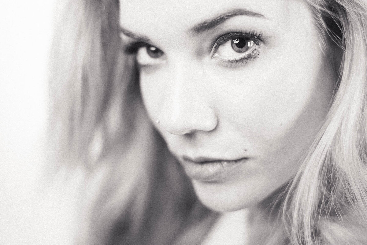 Editorial-style close-up of a woman with hair swept to the side, gazing deeply into the camera with a captivating expression.