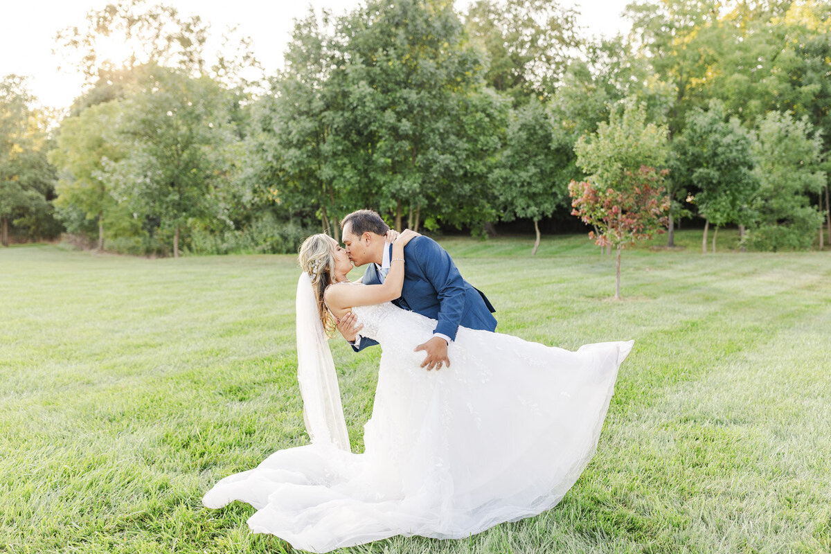 groom dipping and kissing bride on a grassy lawn