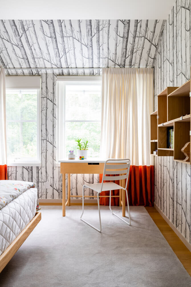 Boston decorators create a modern kids' bedroom with Cole & Son wallpaper, orange drapery, a modern desk and chair, and wall-mounted shelving units.