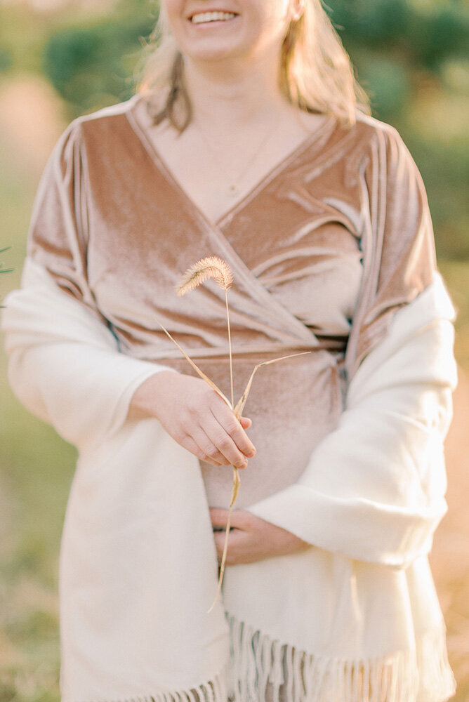 Pregnant woman in pink dress with white shawl holding a cattail