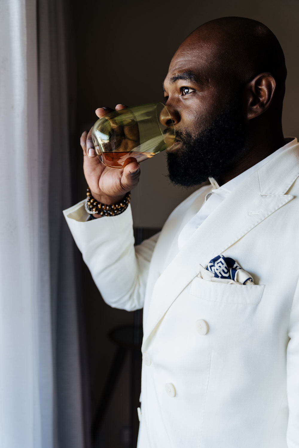 Groom in his white suit drinking from a glass