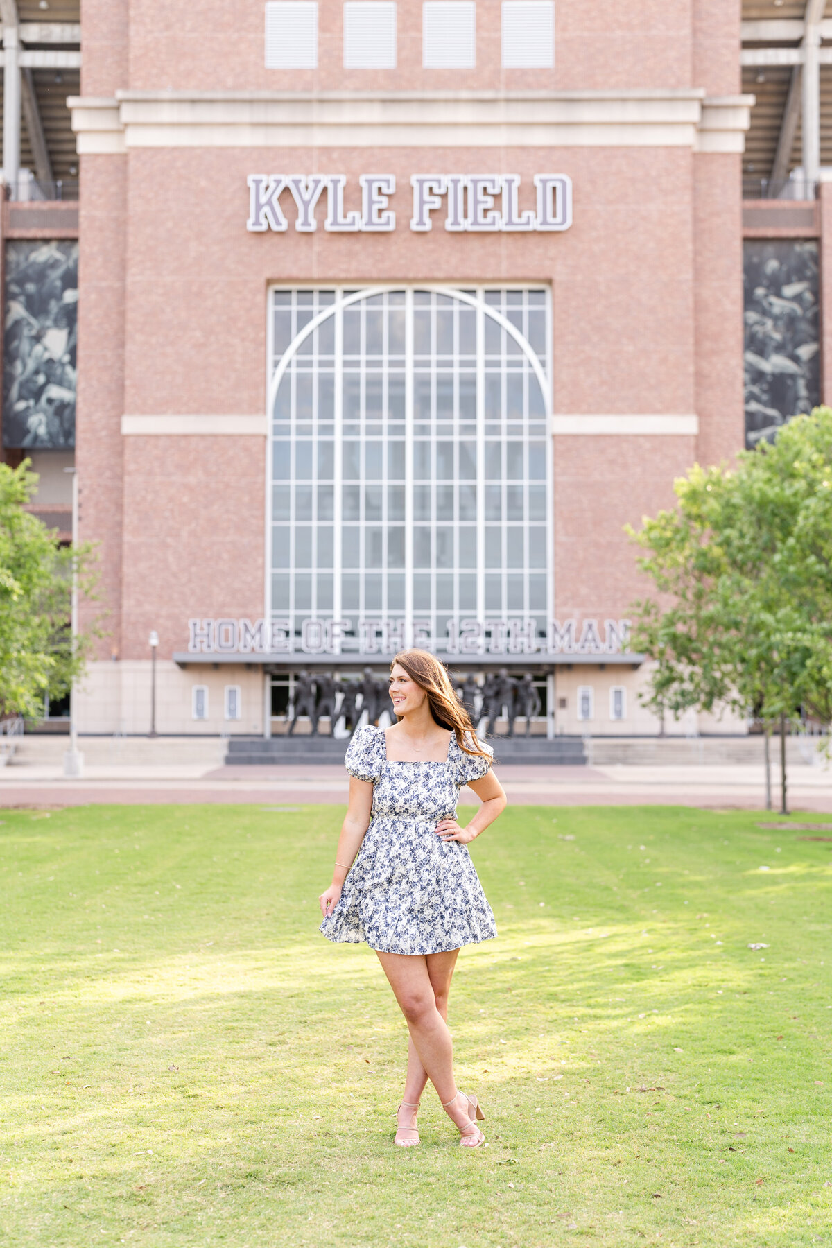 Texas A&M senior girl swishing dress with hand on hip and laughing away in Aggie Park while standing in front of Kyle Field