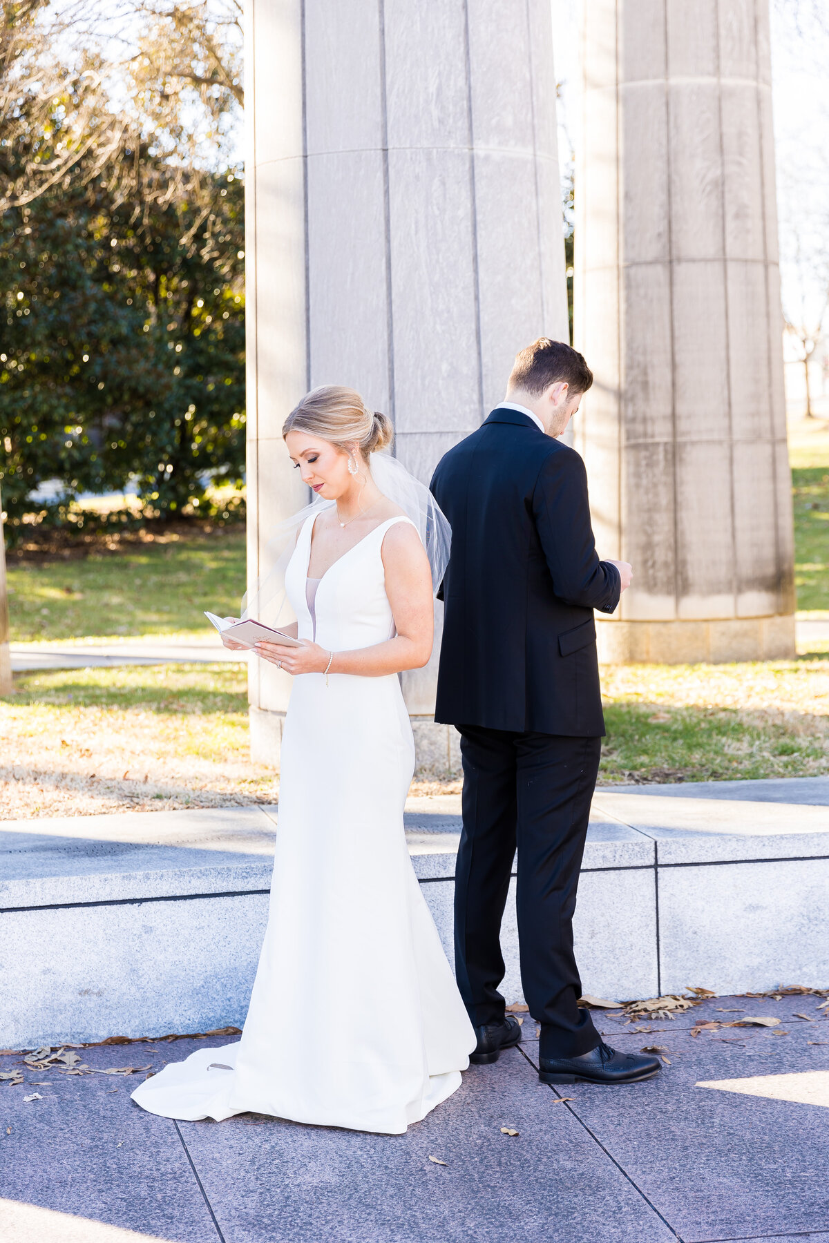 Bride and groom standing back to back reading notes to each other
