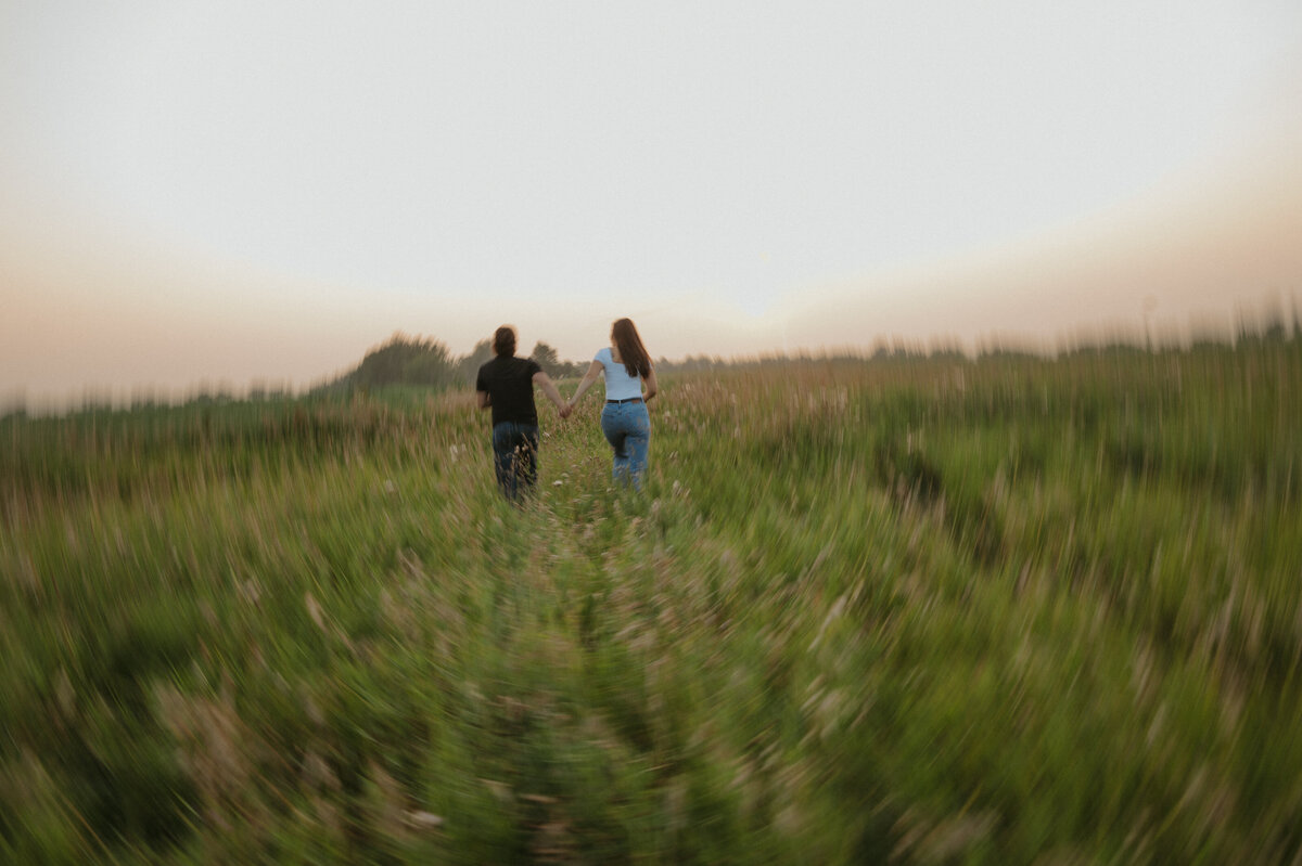 Engaged couple holing hands walking in country field together