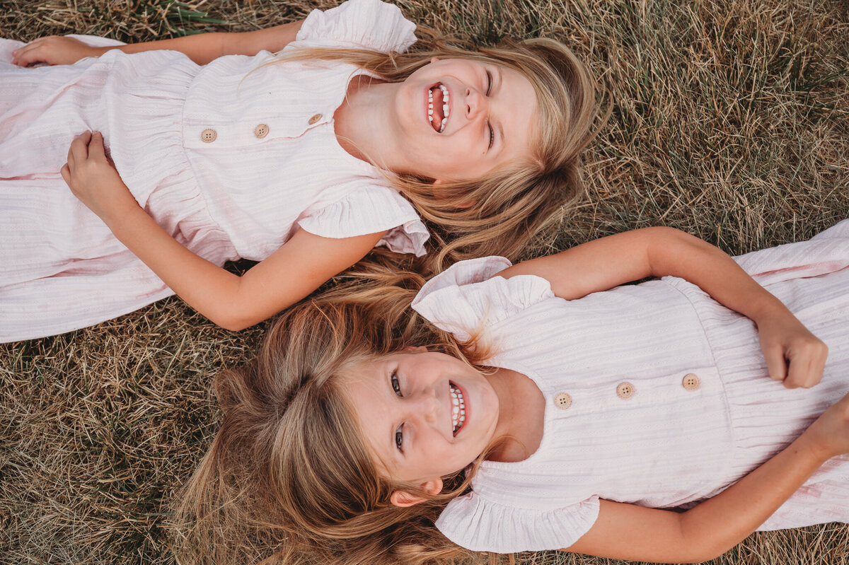 Twin girls lying on ground looking at the sky laughing