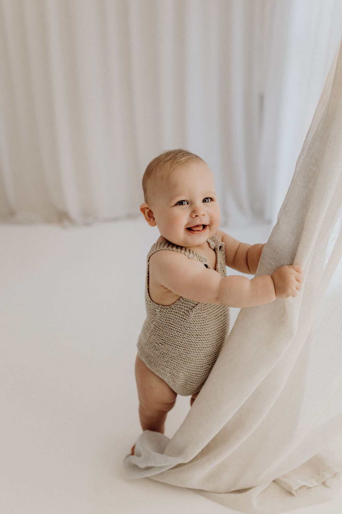 A little baby wearing a beige onesie during a milestone photoshoot in the studio in christchurch with lucy jane photography