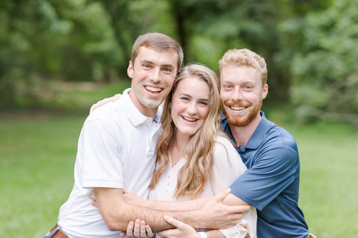 Two brothers hugging their sister tight for a family portrait with big smiles.