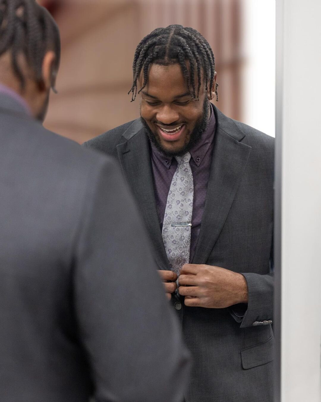A smiling man adjusting his job interview suit jacket in the mirror