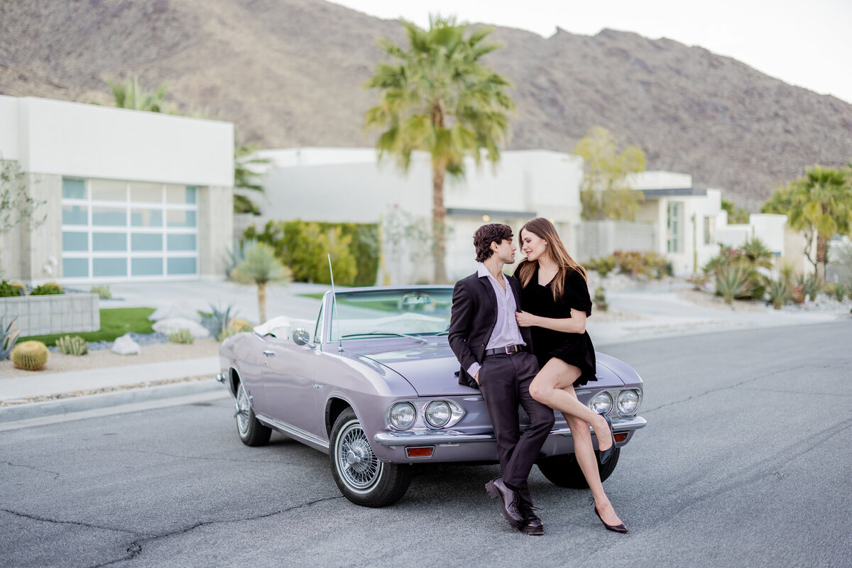 Couple sitting on the hood of a vintage convertible, palms and desert backdrop creating a cinematic Palm Springs moment.