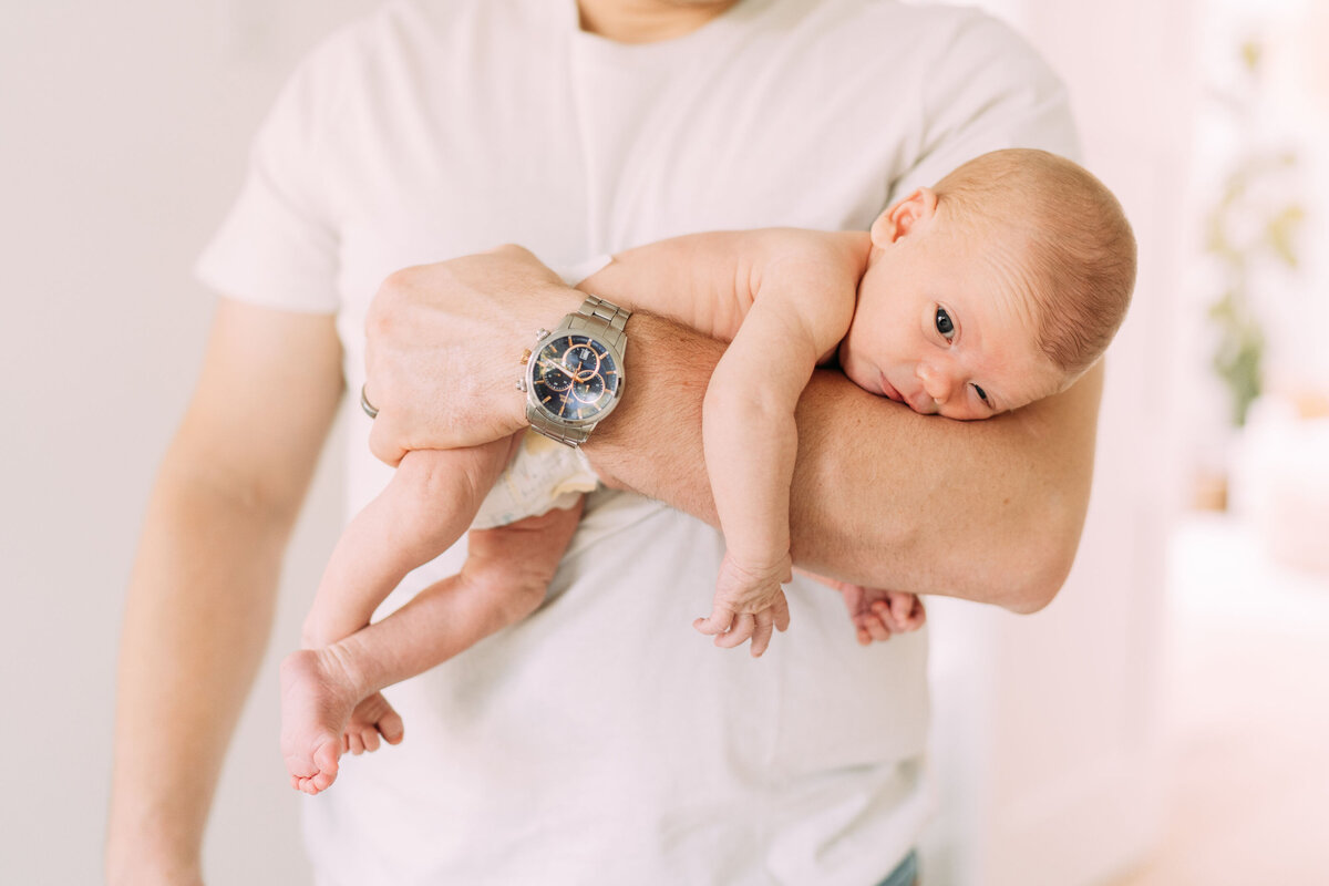 father holds baby boy football style hold