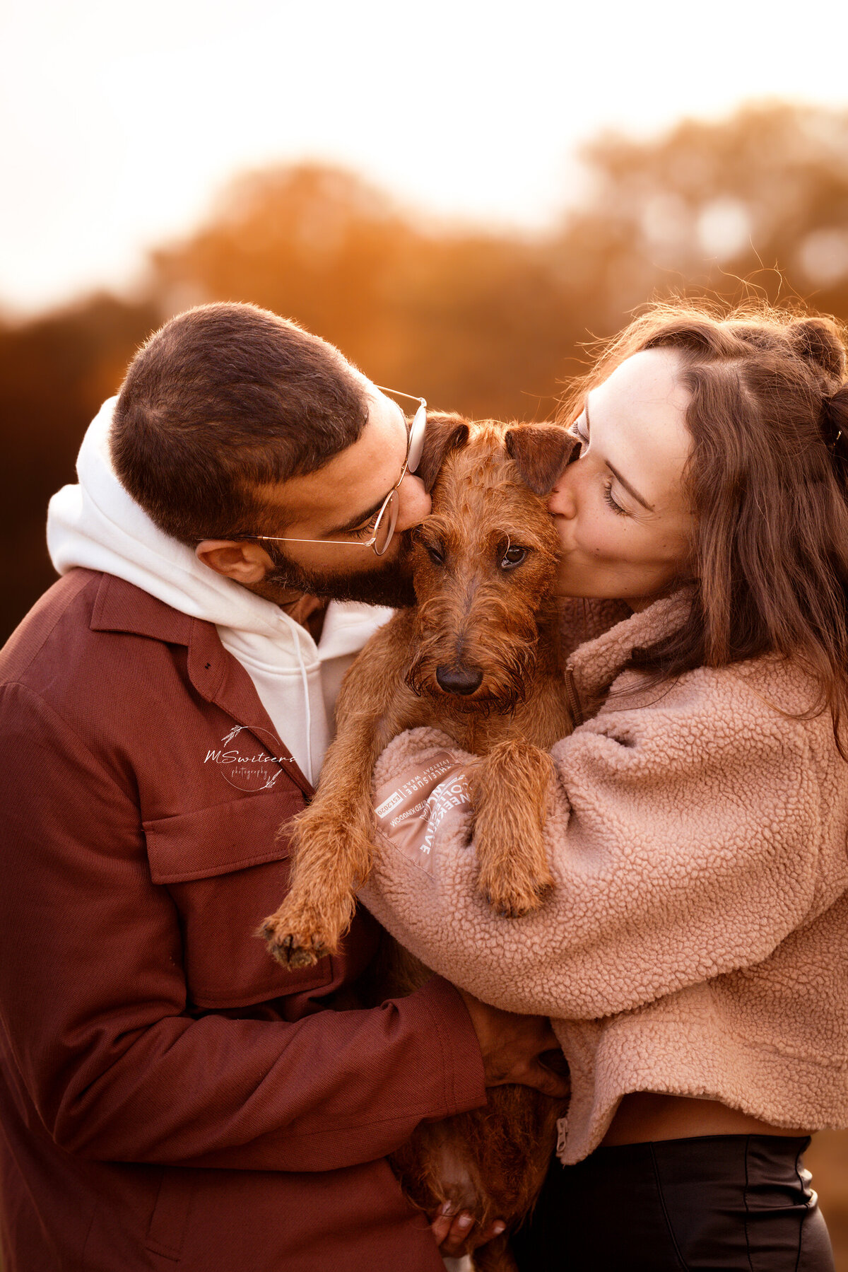 Hond krijgt kus van baasjes tijdens fotoshoot in de heide met zonsondergang. 
