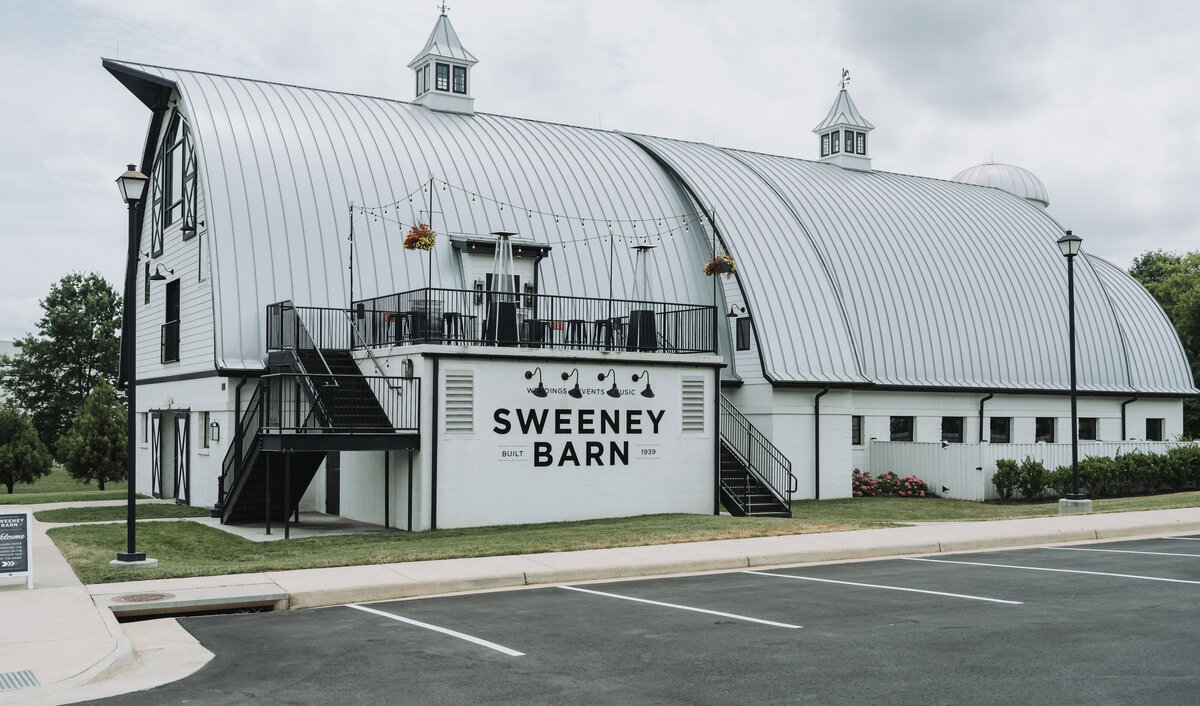 The distinctive white exterior and iconic curved roof of Sweeney Barn, a popular wedding venue in Manassas, Virginia, captured under a cloudy sky by Quinn Photography LLC.