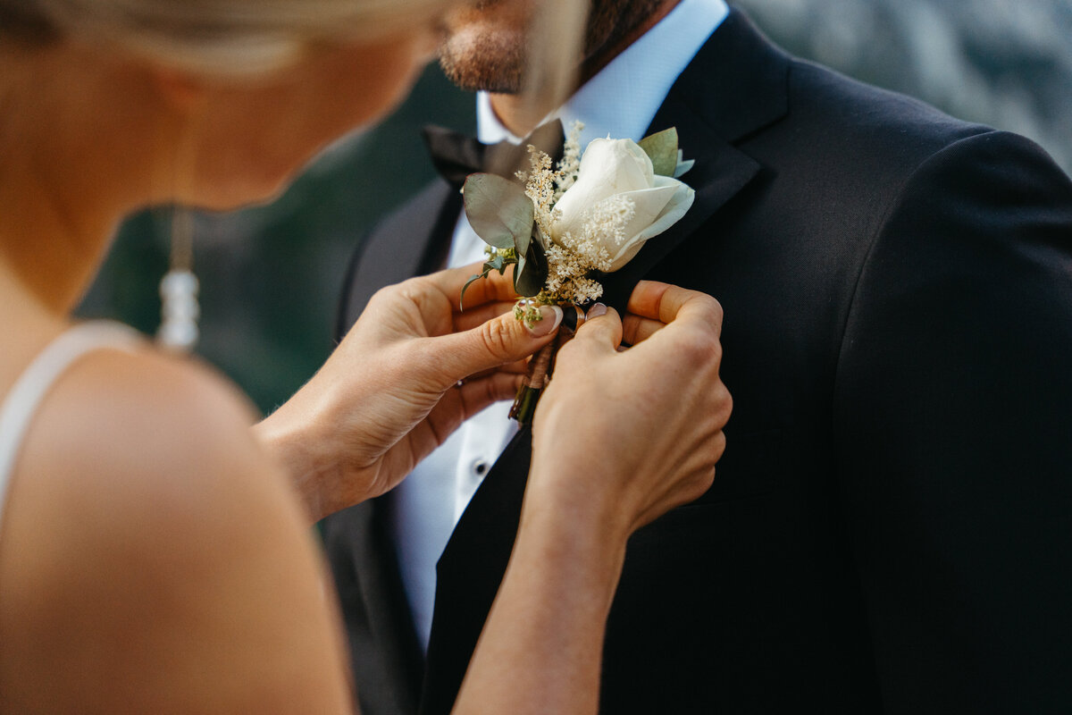 Bride pinning boutonniere on groom’s tuxedo at Lago di Braies