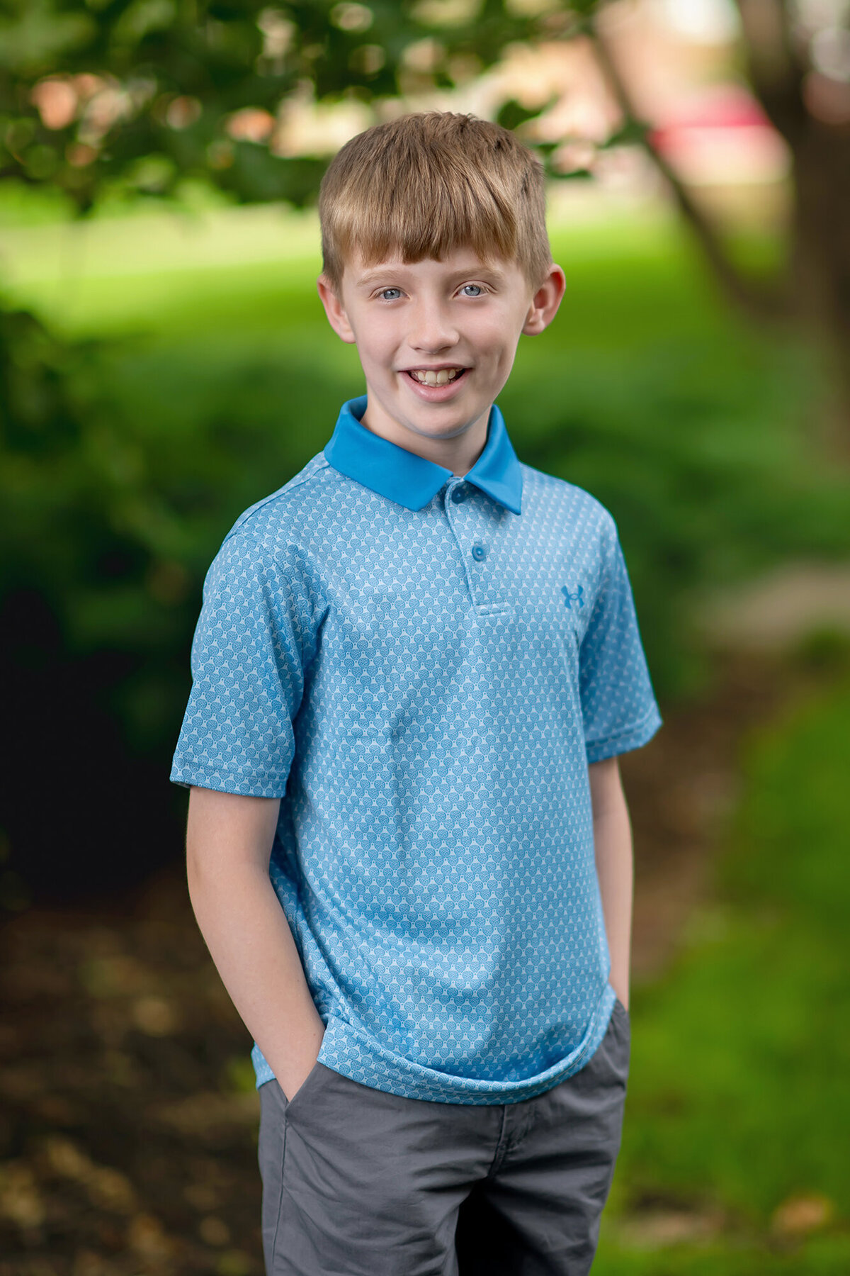 Young boy wears a blue polo and poses in a woodsy area