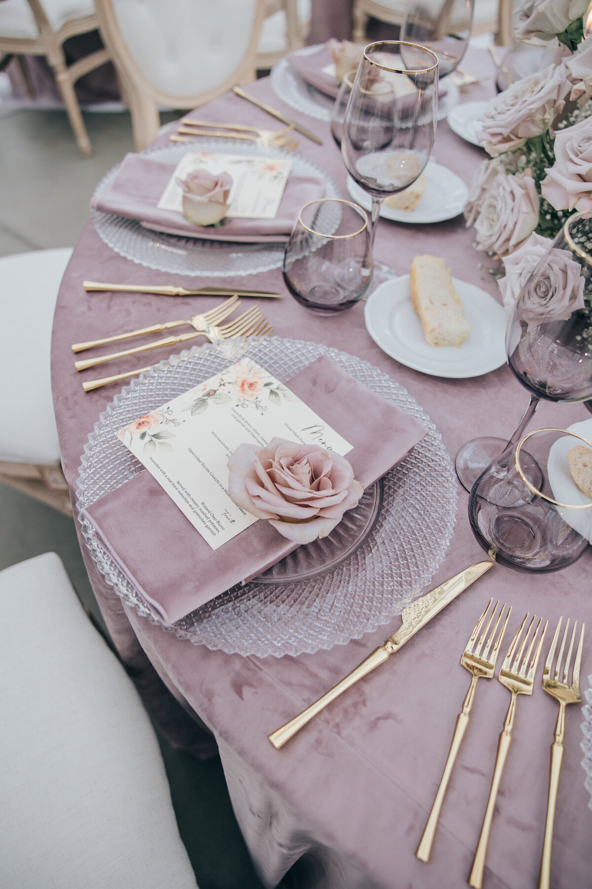 Lavender tablecloth, gold cutlery, and crystal plates for wedding dinner