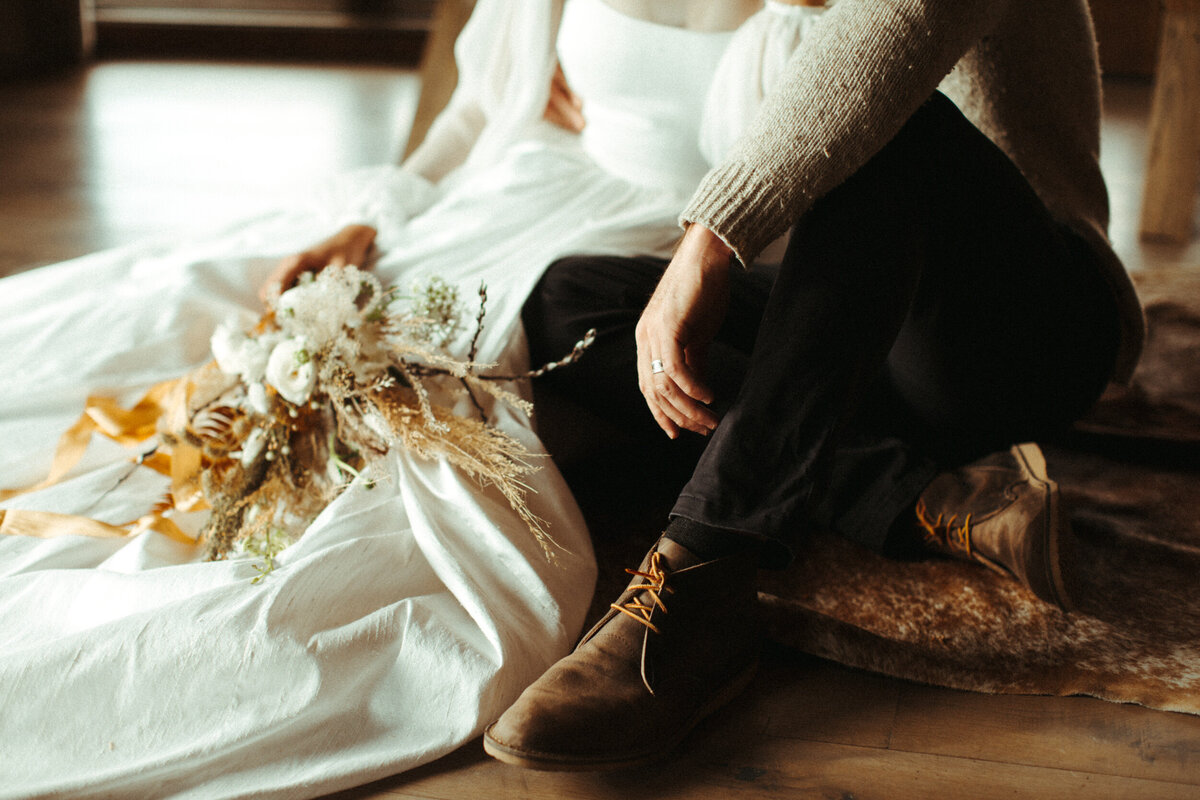 Close up of bouquet sitting in bride's lap as she sits on the floor next to her groom