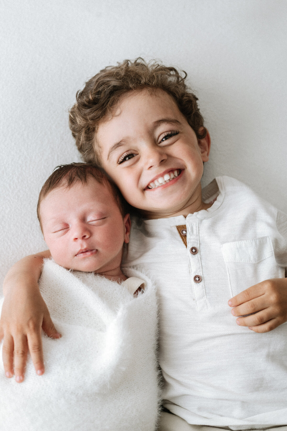 a newborn baby and his brother cuddling and smiling at west sussex newborn photoshoot