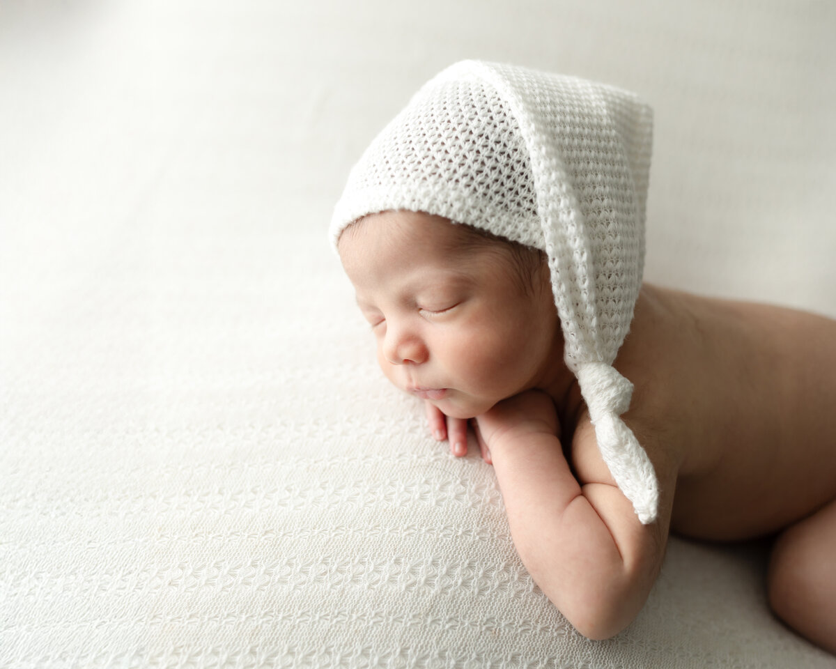 newborn baby boy in white hat posed on white fabric for studio portraits cleveland newborn photographer