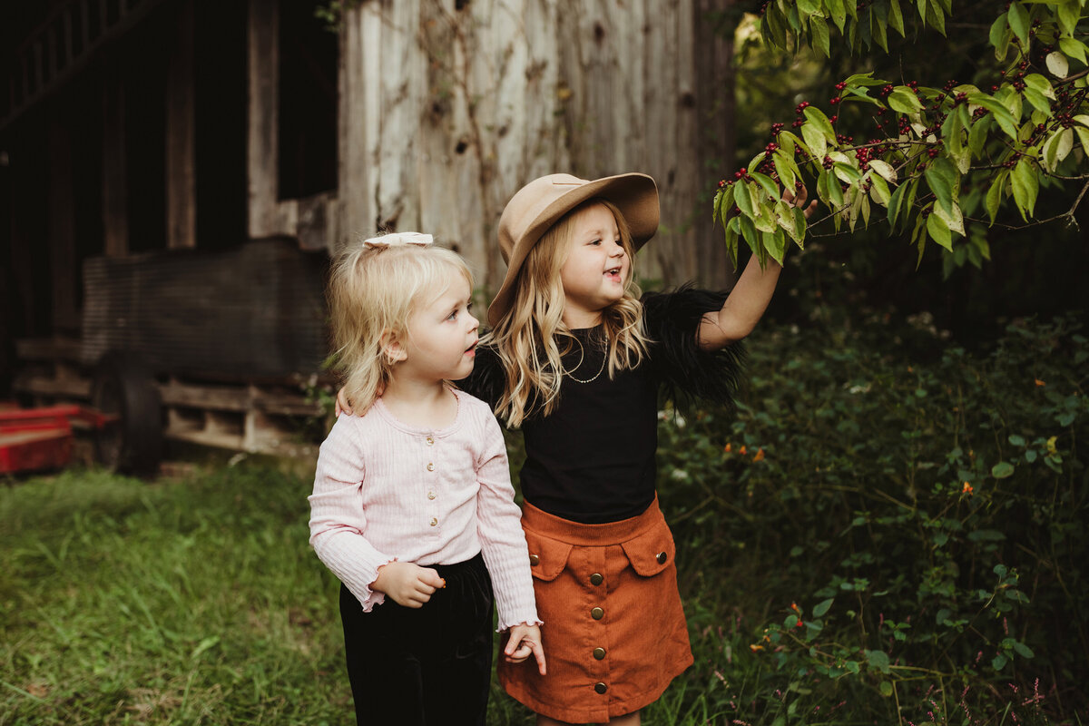 Older sister showing little sister how to pick berries.