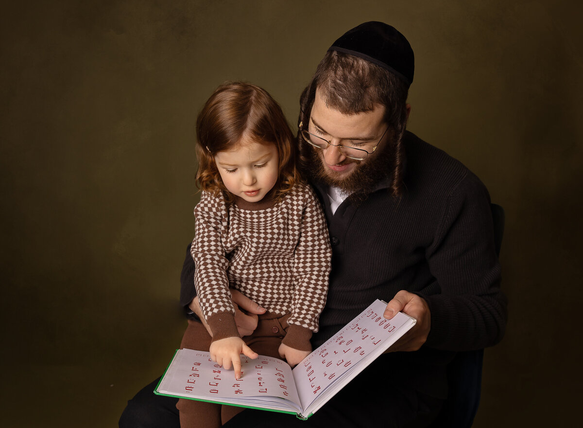 Little boy and his fatehr are captured reading a Hebrew book at a photoshoot to commemorate the little boy's upsherin. Captured by brooklyn family photographer Chaya Bornstein.