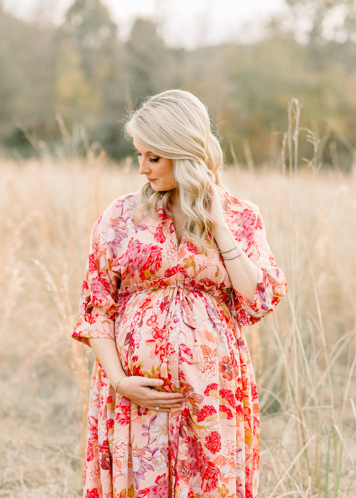 Central Mississippi maternity photographer captures image of mom to be posing in open field in long floral dress.