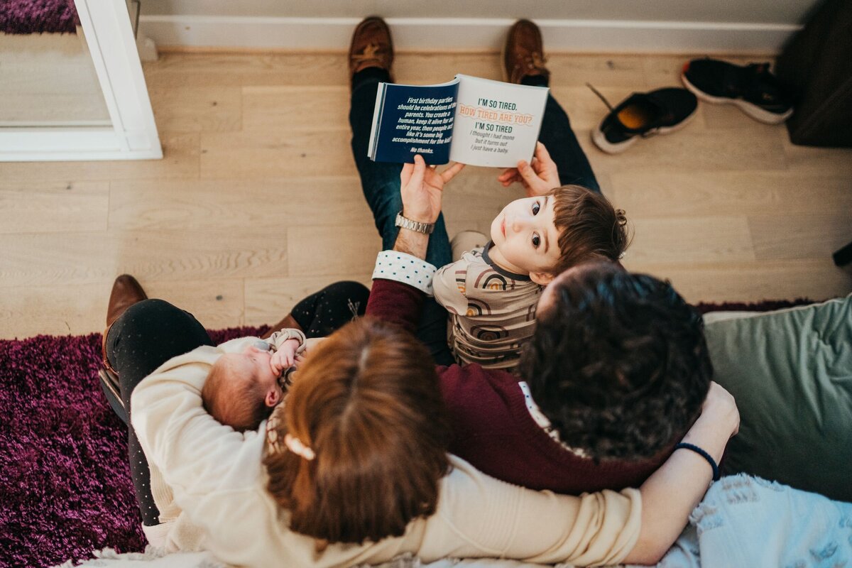 mom-and-dad-reading-to-toddler-while-holding-newborn-baby