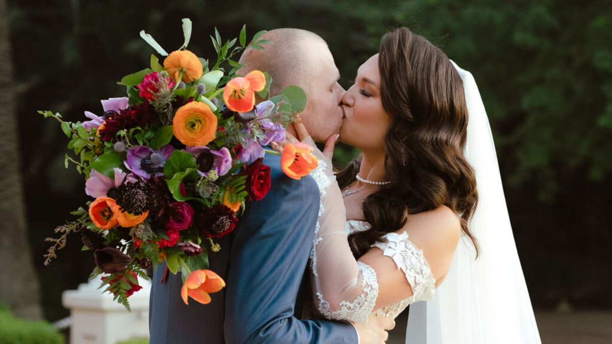 A romantic wedding couple kissing with the bride holding a beautiful bouquet.
