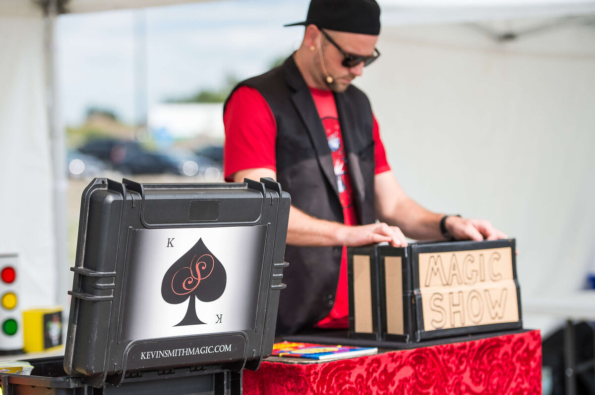 a magician in a red t-shirt doing a trick during a corporate children's event.  Captured by Ottawa Event Photographer JEMMAN Photography COMMERCIAL
