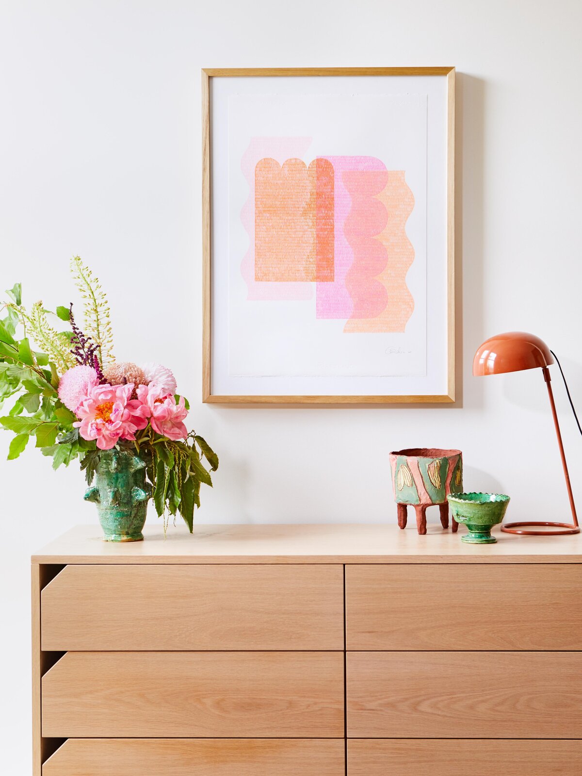 Timber console styled with green ceramics, pink flowers, and modern artwork - hallway by interior stylist in Melbourne