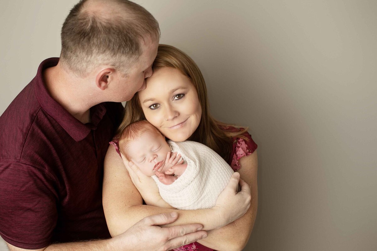 New parents cuddling their newborn in their arms, with soft smiles on their faces