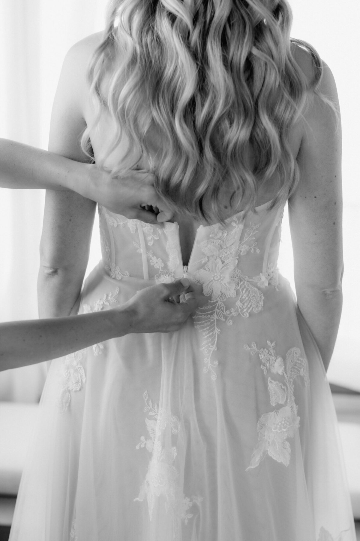 Der letzte Teil des Reisverschlusses am Kleid der Braut wird hier von zwei Händen geschlossen.
