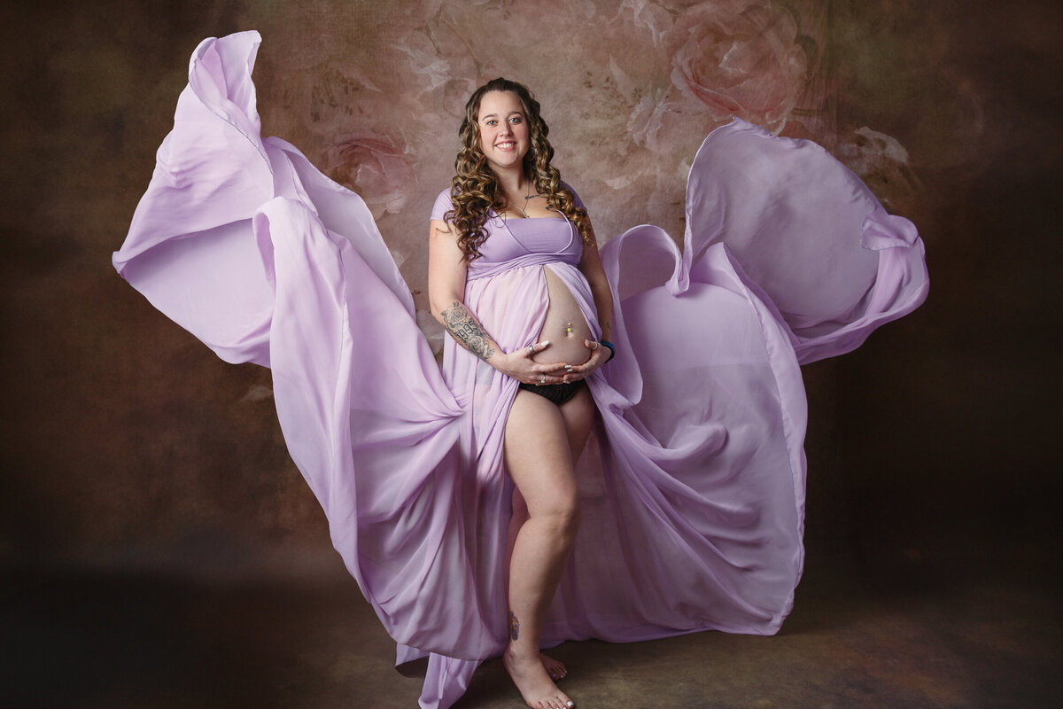 Studio portrait of a woman wearing a purple gown that was that was photographed as the fabric flew up into the air