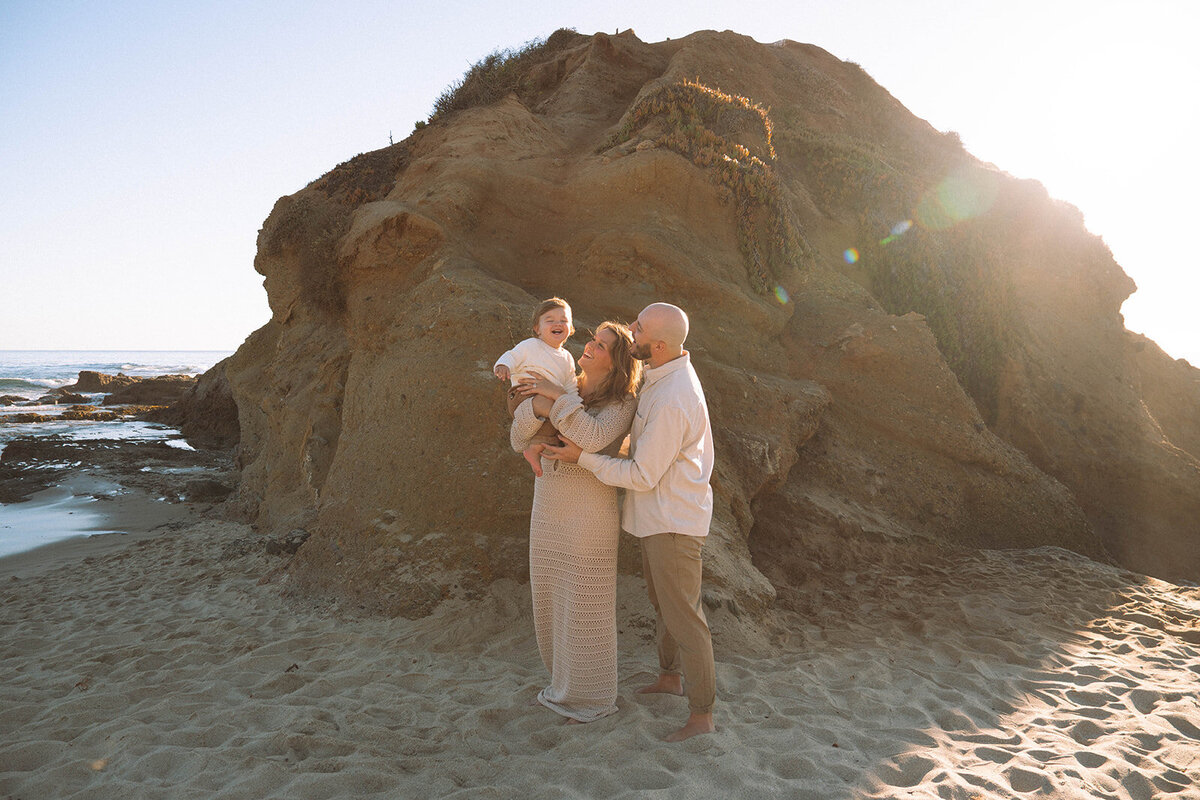 Family laughing together at the base of the cliffs at Goff Cove, Laguna Beach, captured in soft golden light by Orange County photographer Maria Alcantara.