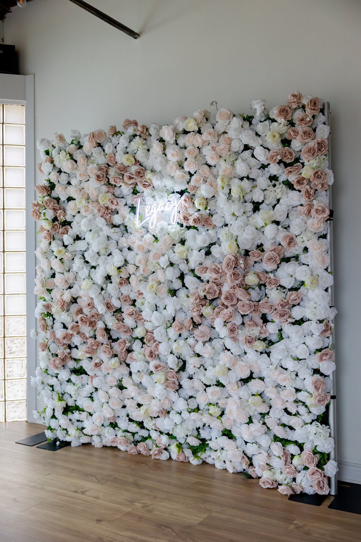 Pink rose floral wall with neon Legacy sign.