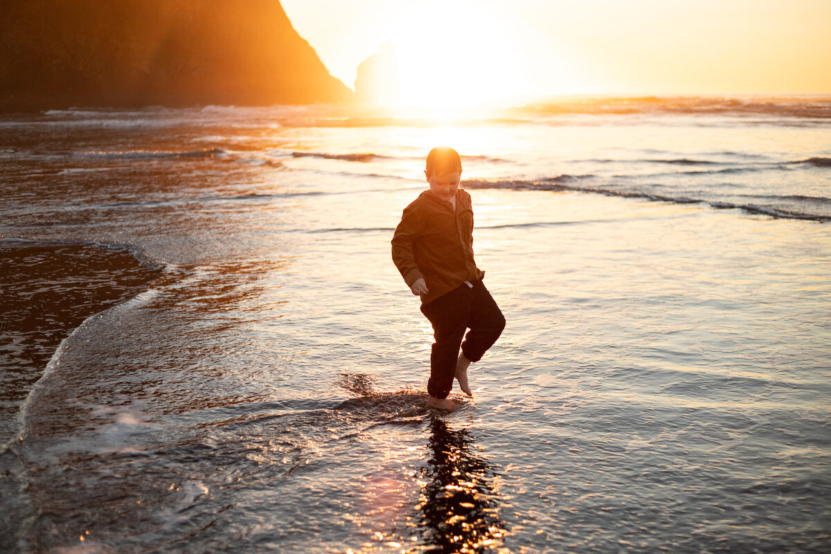 Boy standing at shore in Cannon Beach, Oregon at sunset.