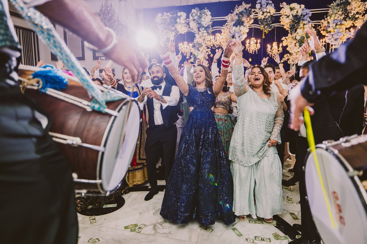 An indian bride and groom dancing to dhol players on the dance floor during their wedding reception