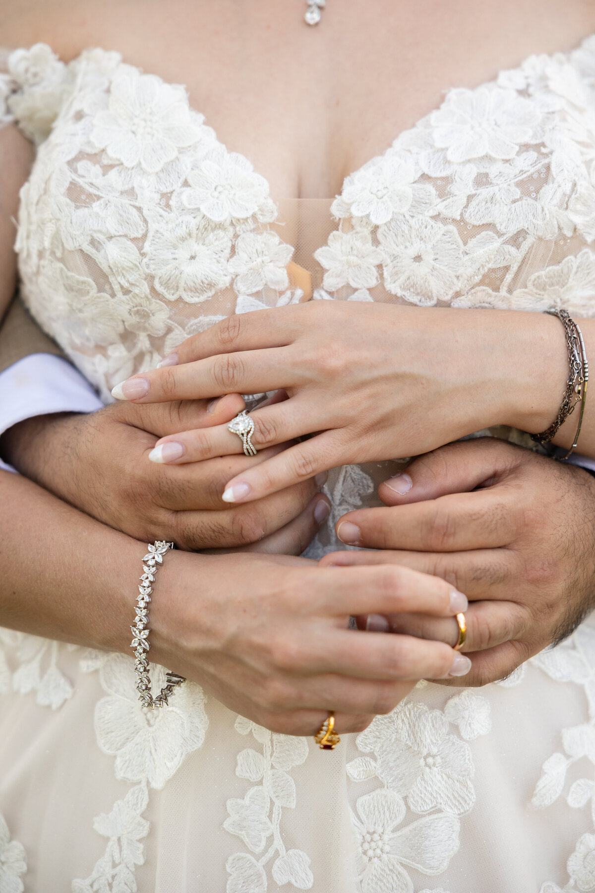 A romantic close-up of the bride and groom’s hands gently intertwined, highlighting their wedding rings and the intricate lace detail of the bride’s gown. Her engagement ring sparkles beside a delicate bracelet, while the groom’s arms wrap lovingly around her waist. This intimate moment was captured by Heartful Films, a Jacksonville wedding photographer and videographer specializing in emotional, detail-rich storytelling.