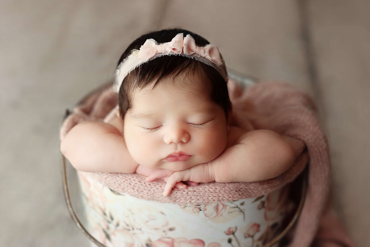 newbonr baby laying in  a  floral bucket wearing  a  headband at a sterling va photo shoot