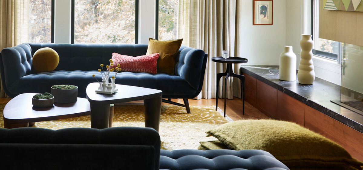 This formal living room, as seen in Boston Globe Magazine by Boston designer Sarah Scales, features black velvet sofas, a custom olive and cream wool rug, alpaca wool floor pillows, and a mix of olive and salmon velvet throw pillows. Neutral walls and window treatments complete the design.