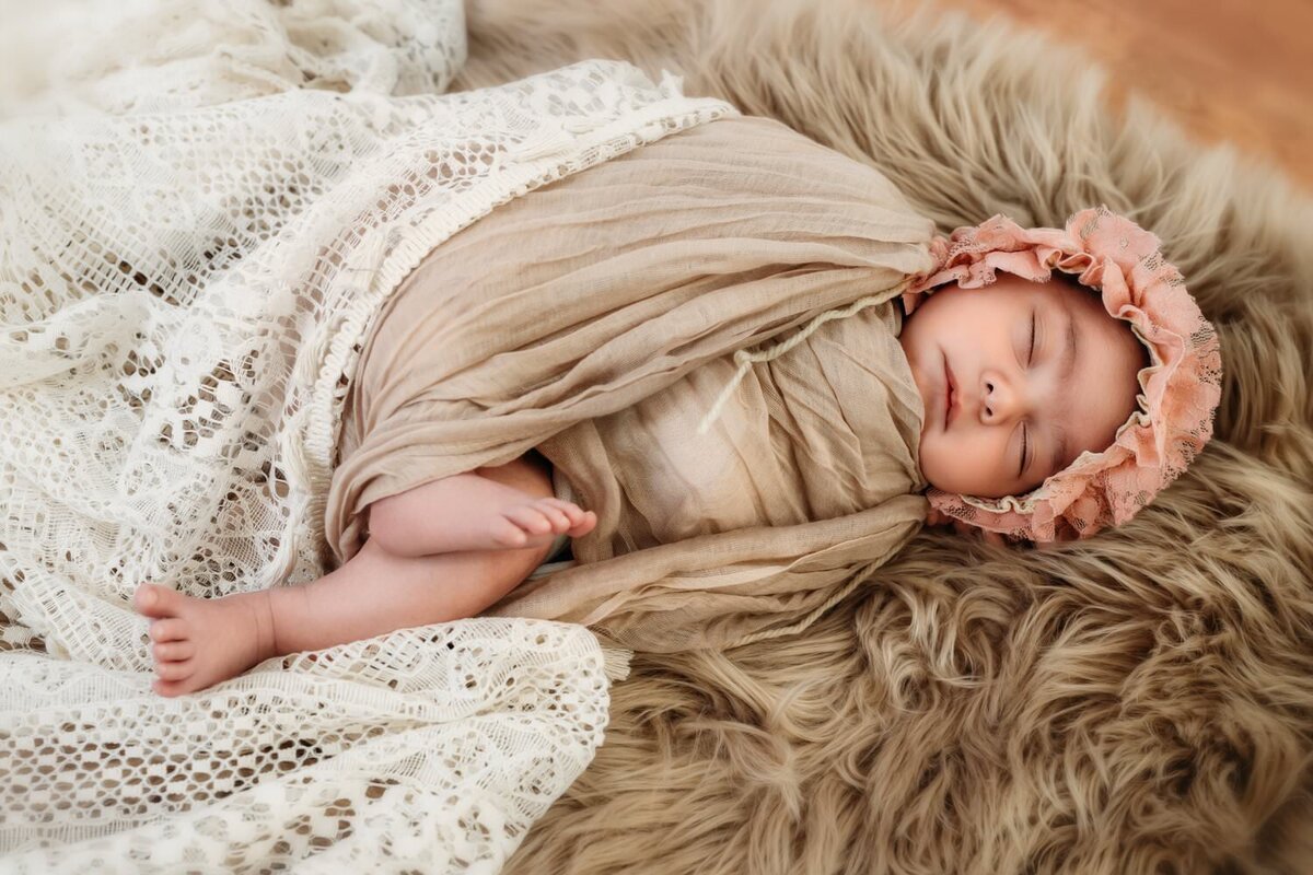 tiny baby in pink lace bonnet during a studio photo session