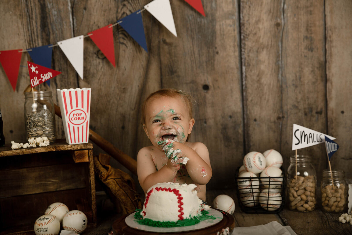 1 year old boy eating his baseball cake. Baseball themed decorations in the background.