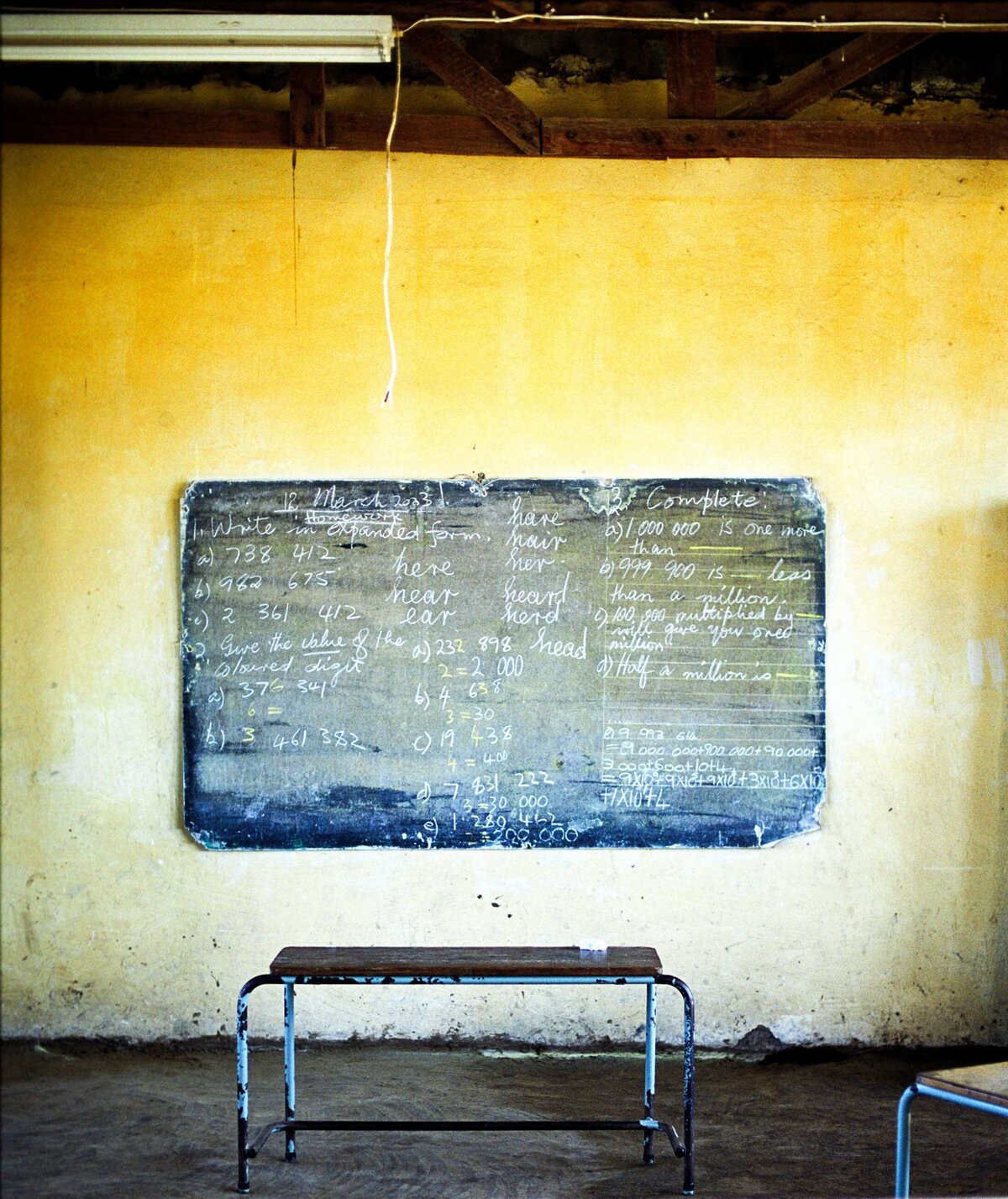 A math formula filled blackboard with yellow wall and old desk show the persistance of education as a means of empowerment and self-transformation