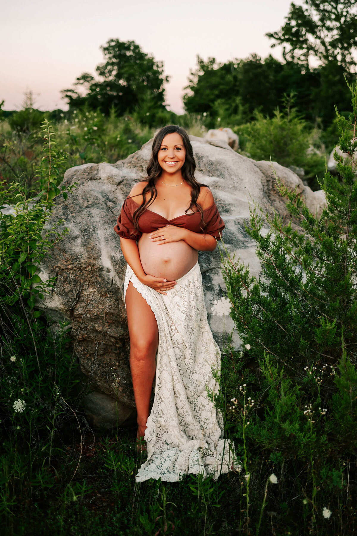 maternity photo of mom leaning against rock outdoors holding baby bump in Branson
