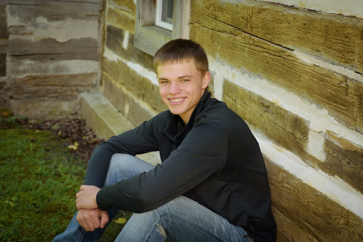 Luxemburg Casco high school senior boy wearing a long sleeve black shirt and jeans leaning against barn wood wall at Devil's River Campground near Green Bay, Wisconsin